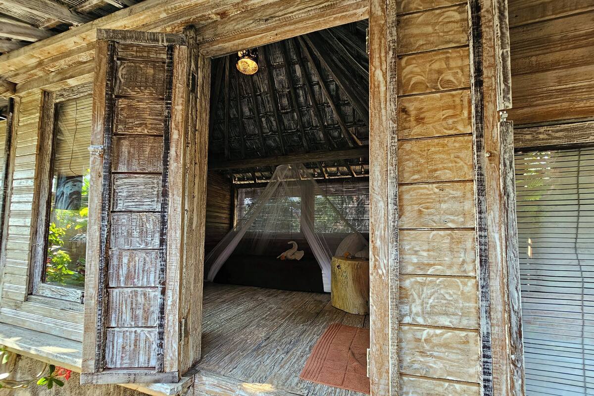 A rustic wooden structure with a partially open door revealing a bed with a canopy.