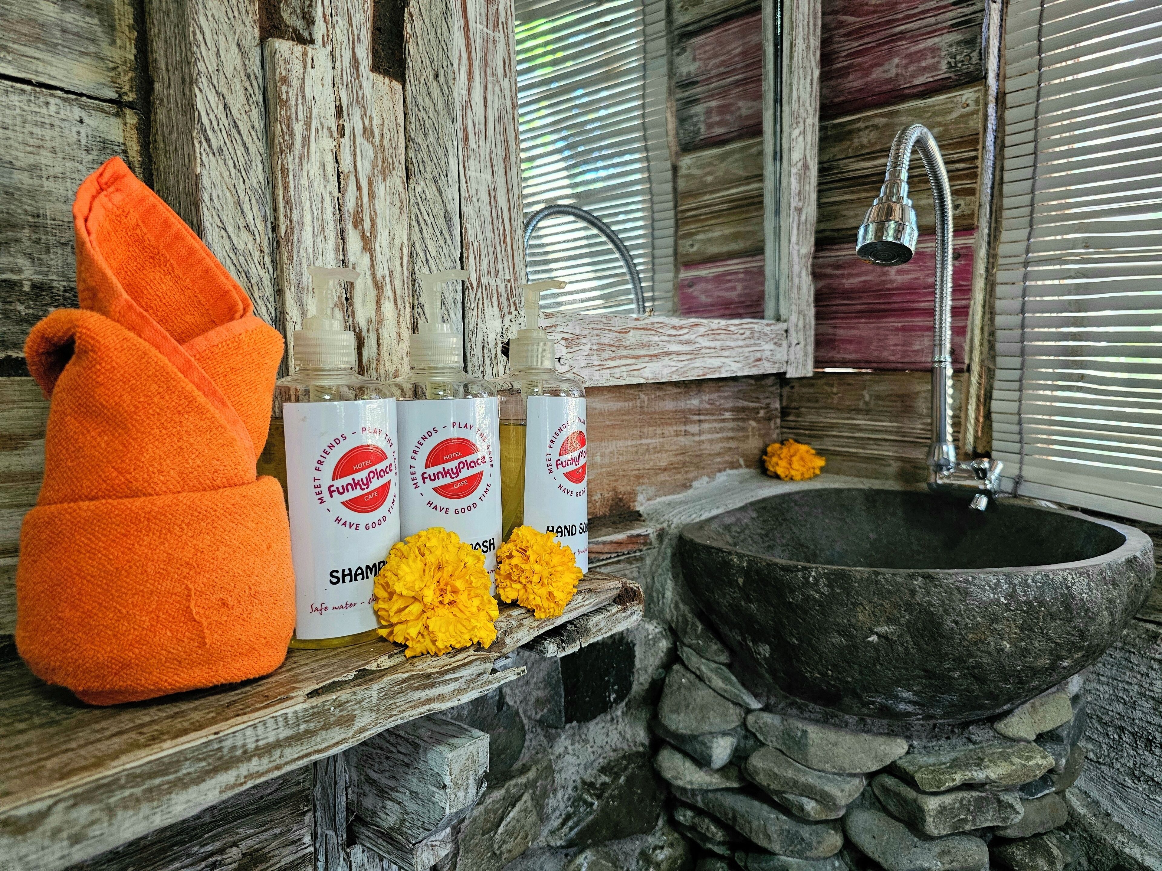 A bathroom with a stone sink, a wooden shelf with a towel, and bottles of shampoo.