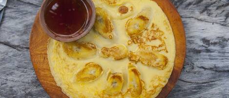 A round wooden plate with a pancake and a small bowl of syrup.