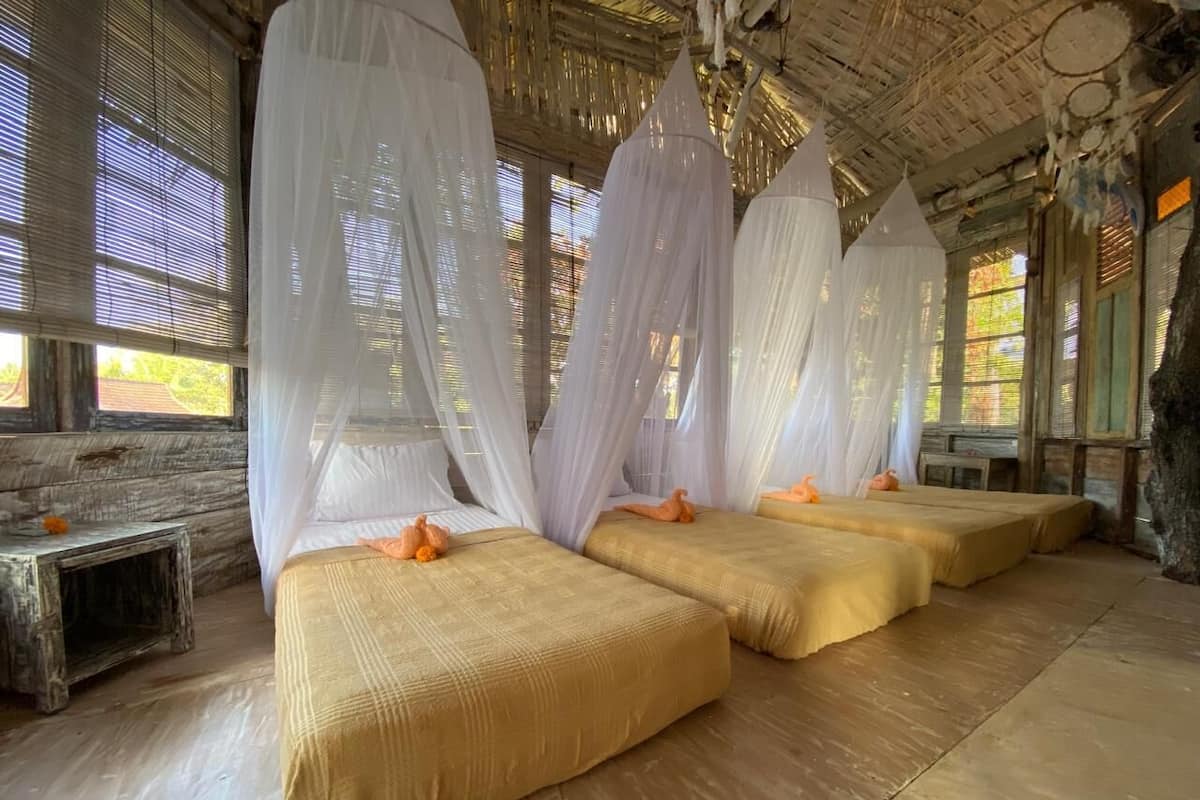 A room with four beds, each with a canopy and orange decorative pillows.