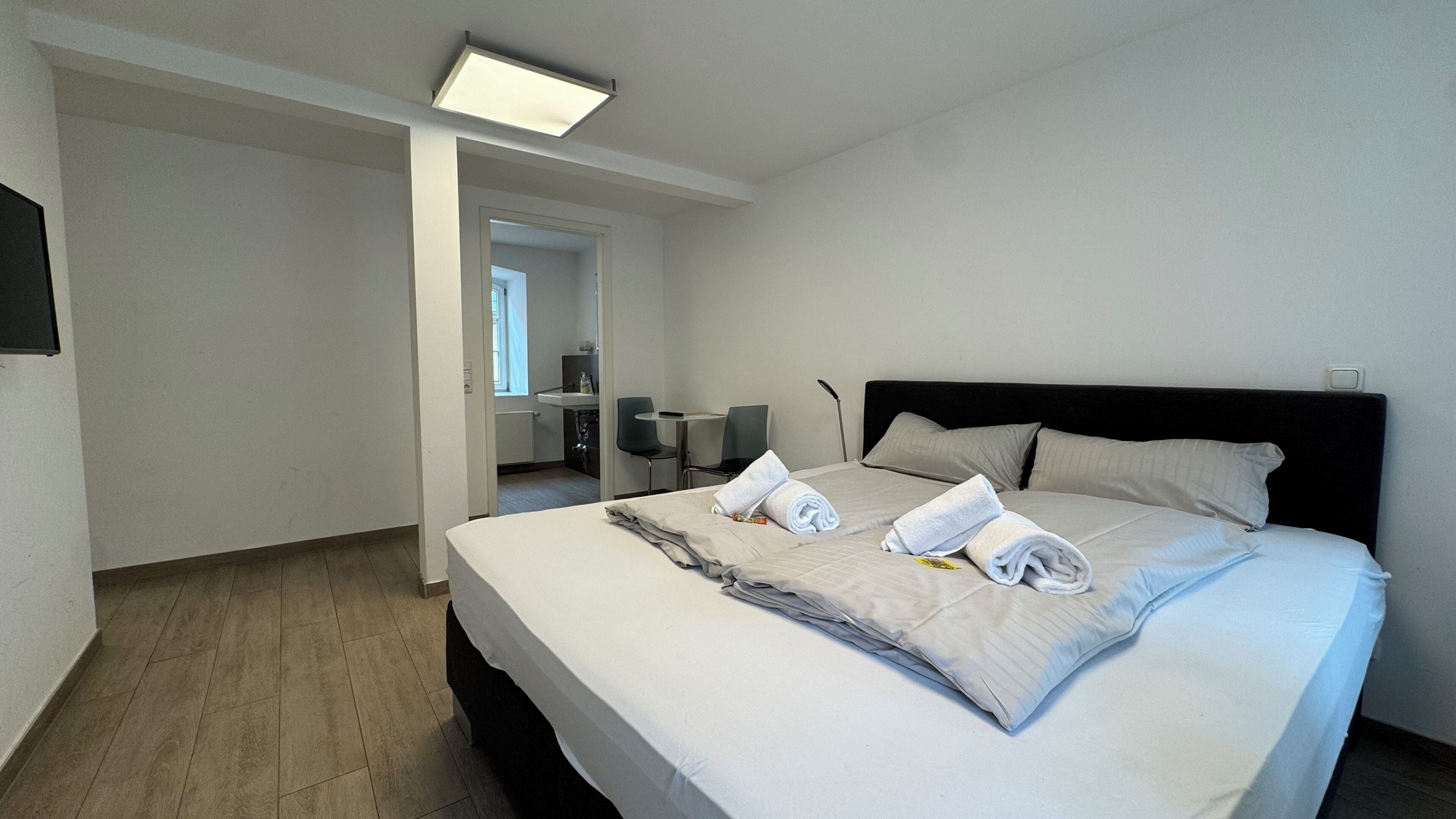 A hotel room with a bed, a desk, a chair, and a bathroom visible through an open door.
