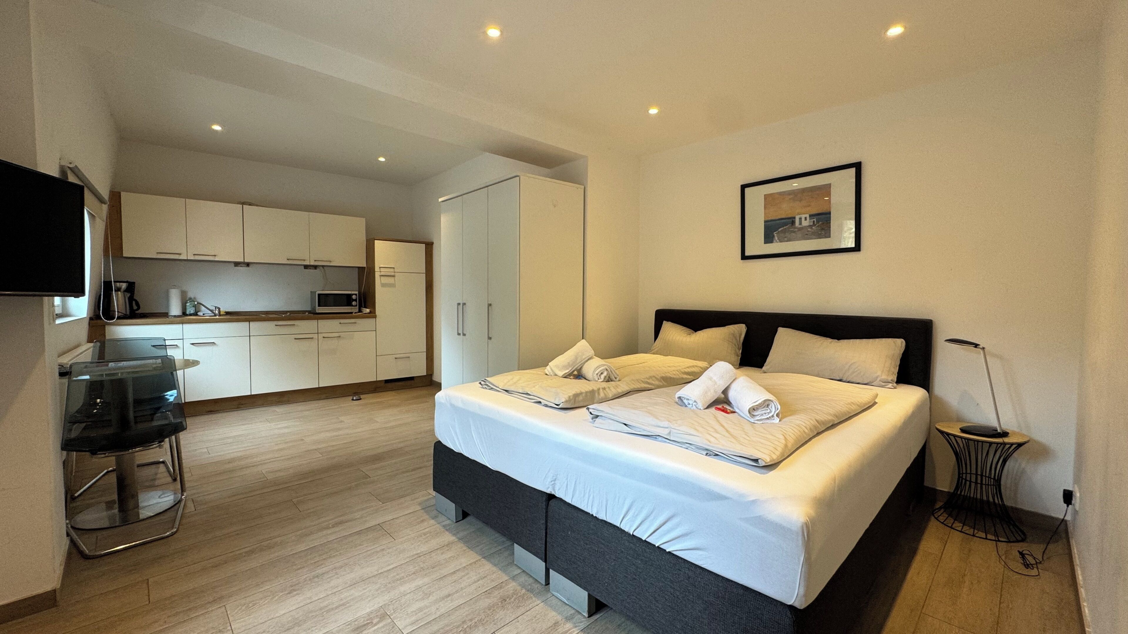 Habitación de hotel con cama, kitchenette, televisor de pantalla plana y un cuadro en la pared.