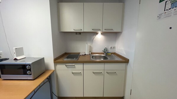A compact kitchenette with a microwave, a sink, and a countertop.