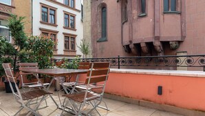 An outdoor dining area with a table and chairs, a railing, and a building with arched windows in the background. - Hotel Havana (Mainz)