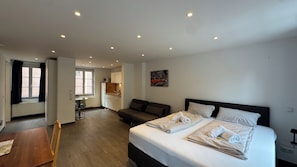 A hotel room with a bed, a sofa, a dining table, and a kitchen area. - Hotel Havana (Mainz)