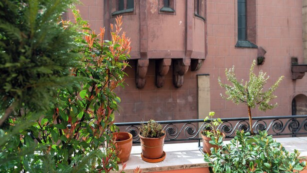 A balcony with terracotta pots, a wrought iron railing, and a building with arched windows in the background. - Hotel Havana (Mainz)