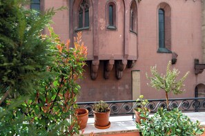 A balcony with terracotta pots, a wrought iron railing, and a building with arched windows in the background.