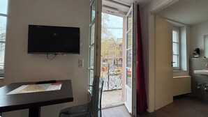 A room with a flat-screen TV mounted on the wall, a table with a map, a door leading to an outdoor area, and a bathroom with a sink and mirror. - Hotel Havana (Mainz)