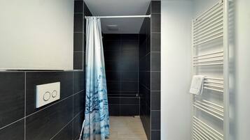 Ein modernes Badezimmer mit dunklen Fliesen, einer Duschvorhang, einem Handtuchhalter und einer Bedienkonsole.