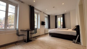 A modern hotel room with a bed, desk, chair, TV, and large windows. - Hotel Havana (Mainz)