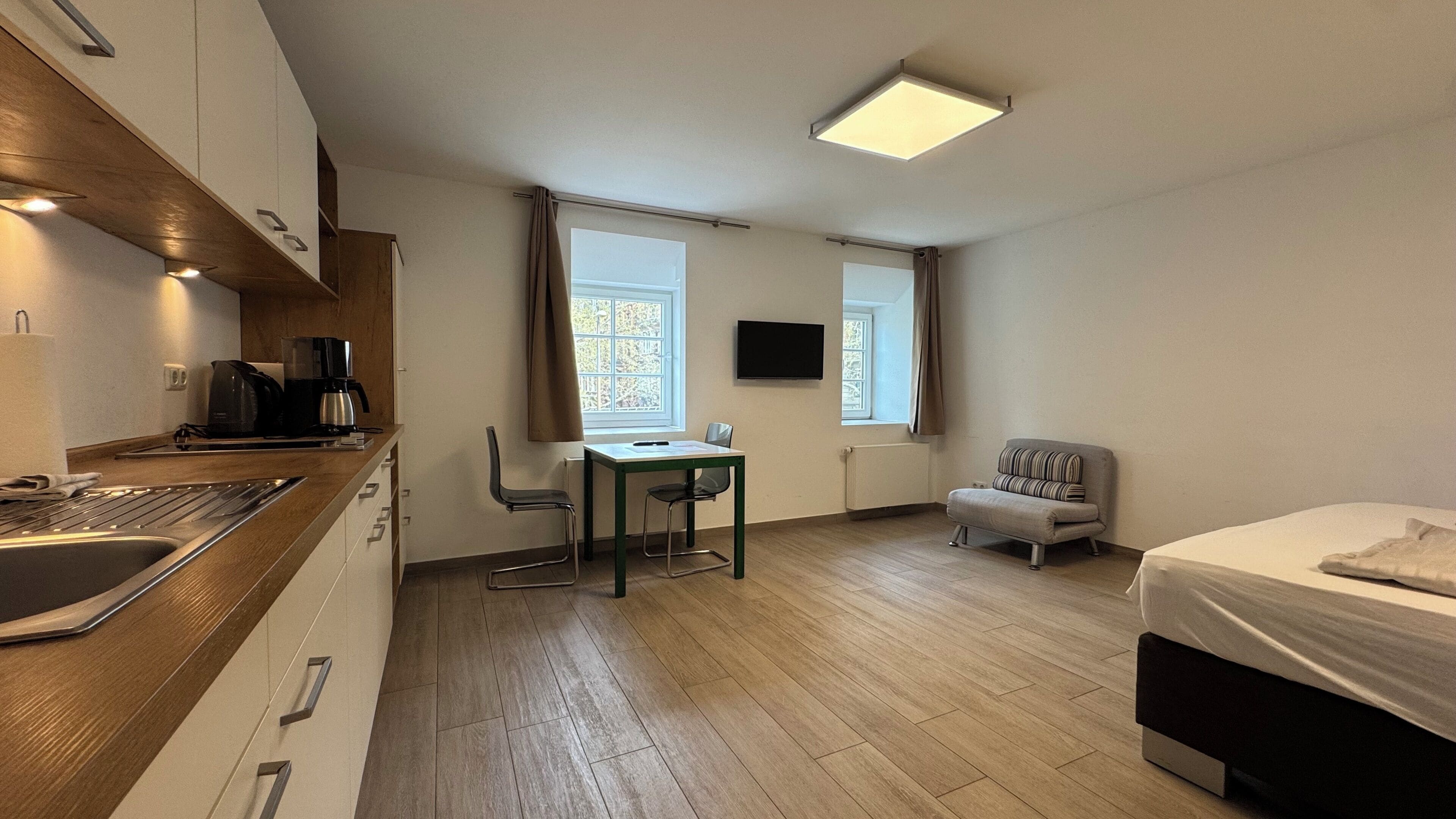 A compact room with a kitchenette, a dining area, a bed, and a TV.