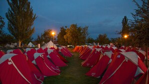 Une rangée de tentes rouges et blanches est disposée sur un terrain de camping.