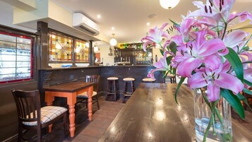 Una zona de bar con taburetes, una mesa de madera y un jarrón de lirios rosados.