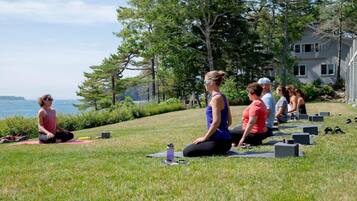A group of people performing yoga on grass near a body of water and trees.