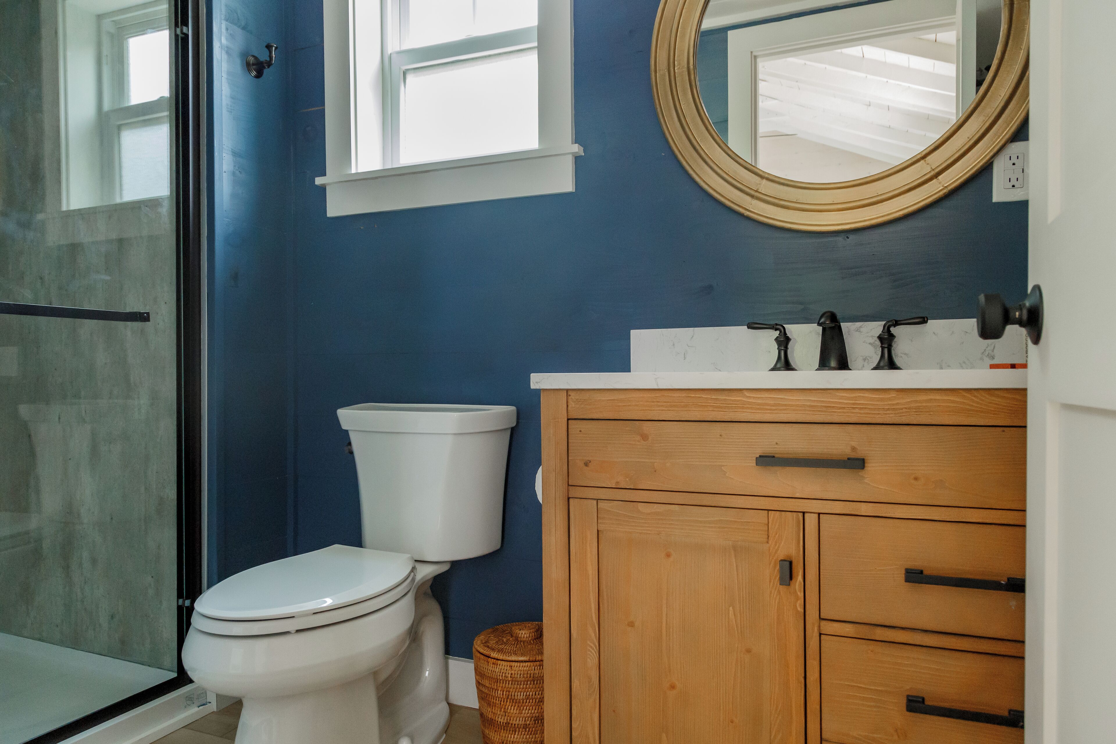 Un baño con pared azul, tocador de madera, inodoro blanco y cabina de ducha de vidrio.