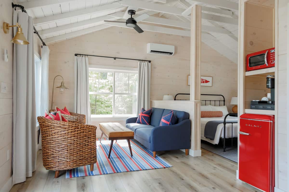 Une pièce confortable avec un lit, un canapé bleu, un fauteuil en osier, une petite table et un réfrigérateur rouge.