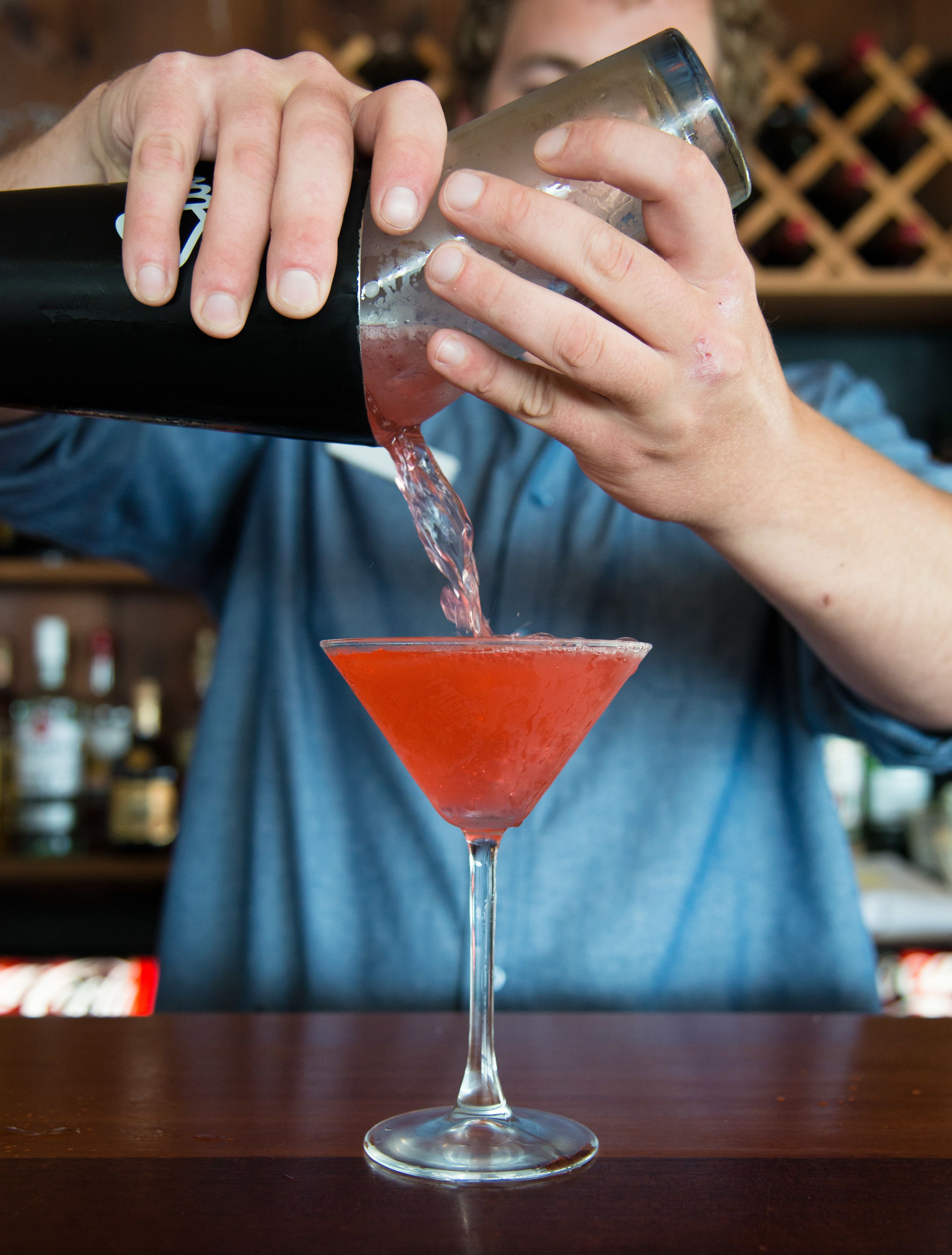 En bartender häller en röd vätska i ett martiniglas.