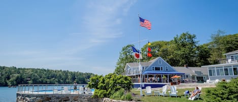 A waterfront property with a pool, outdoor seating, and a flagpole with multiple flags.