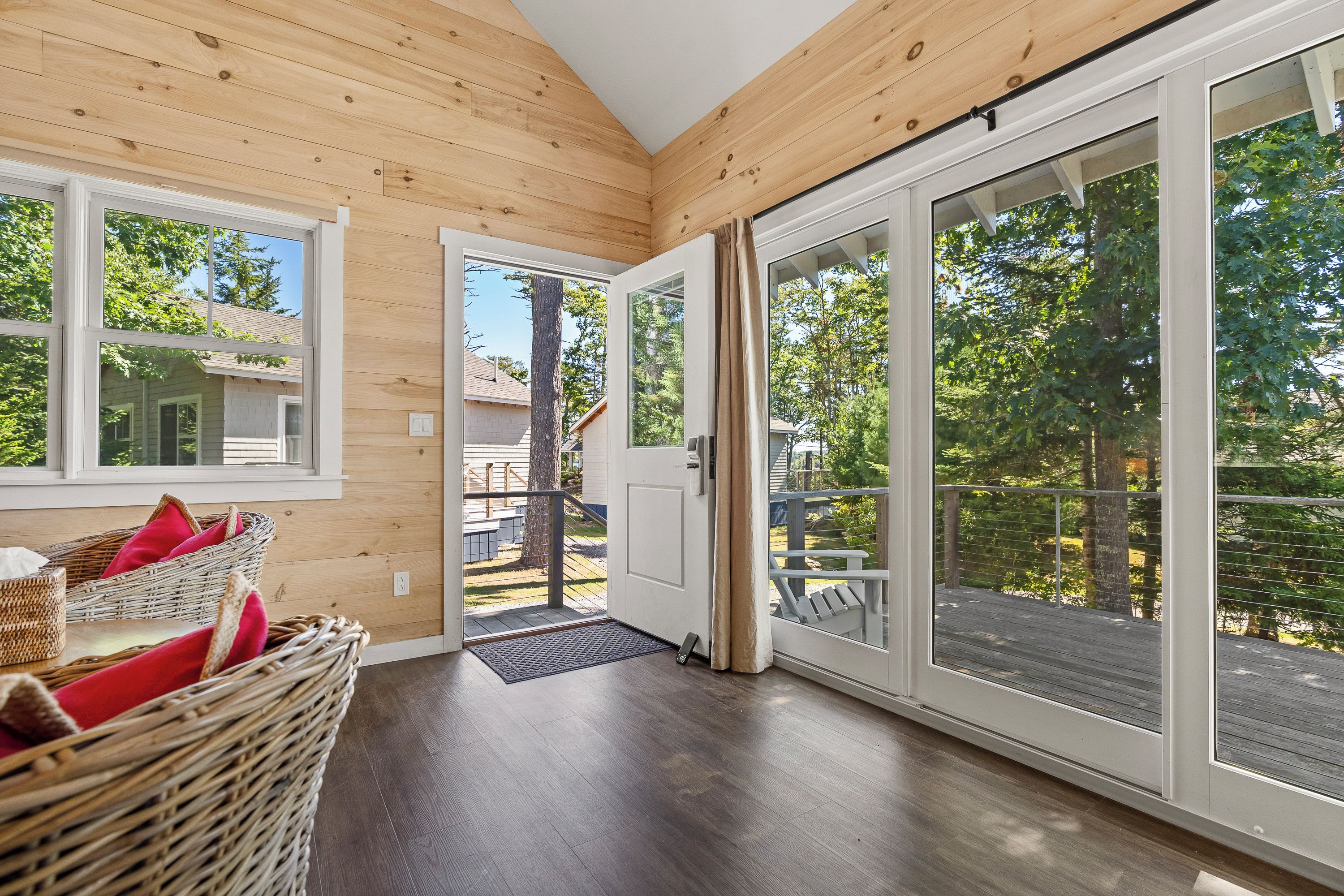 A room with wooden panel walls, a large sliding glass door leading outside, a wicker chair with cushions, and a small table.