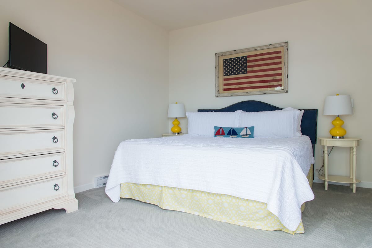 Une chambre à coucher bien rangée, avec un lit, une commode et un drapeau américain accroché au mur.
