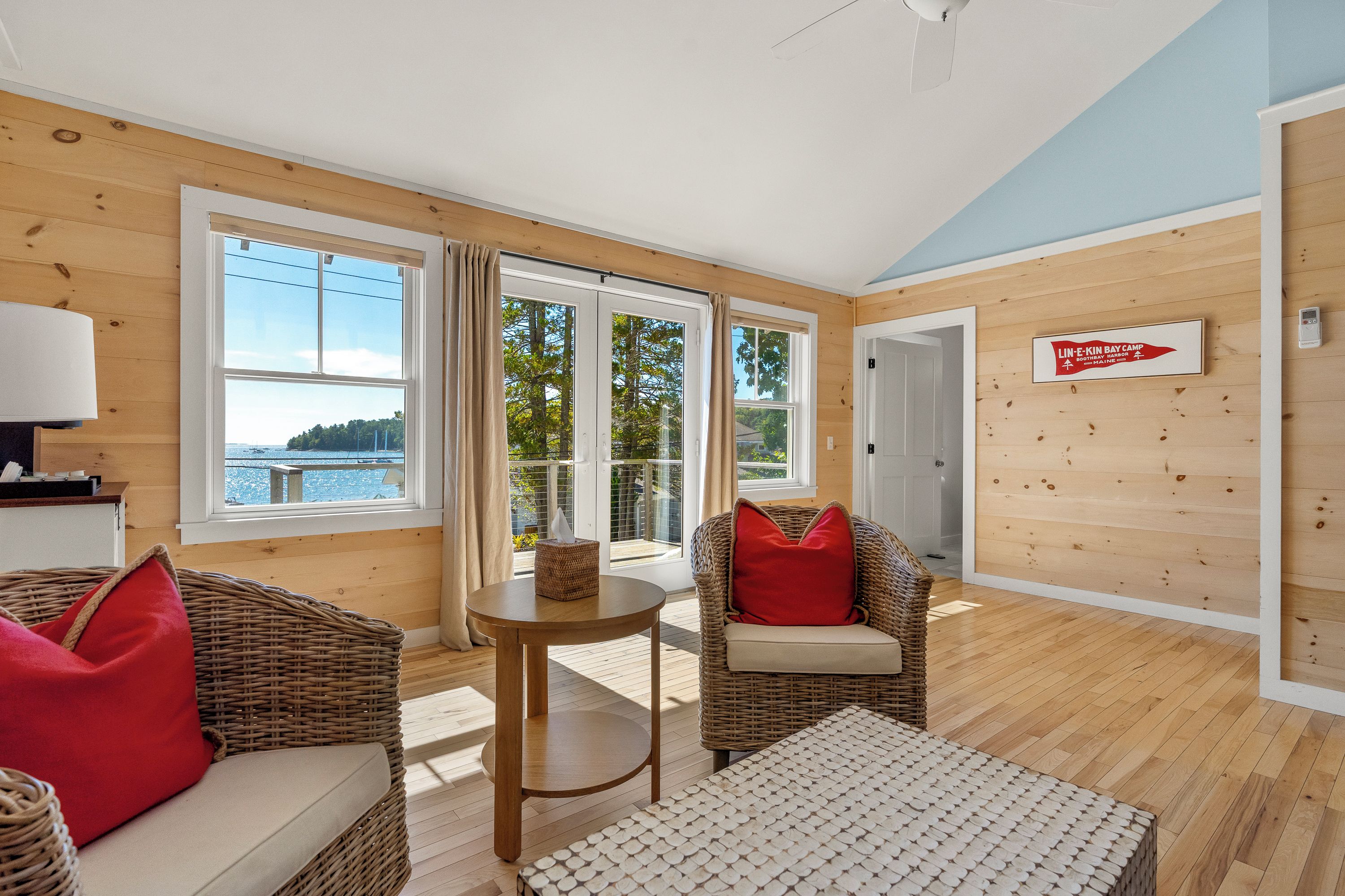 A cabin interior with a large window, wicker furniture, and a sign indicating a camp location.