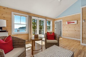 A cabin interior with a large window, wicker furniture, and a sign indicating a camp location. - Linekin Bay Resort (Boothbay Harbor)