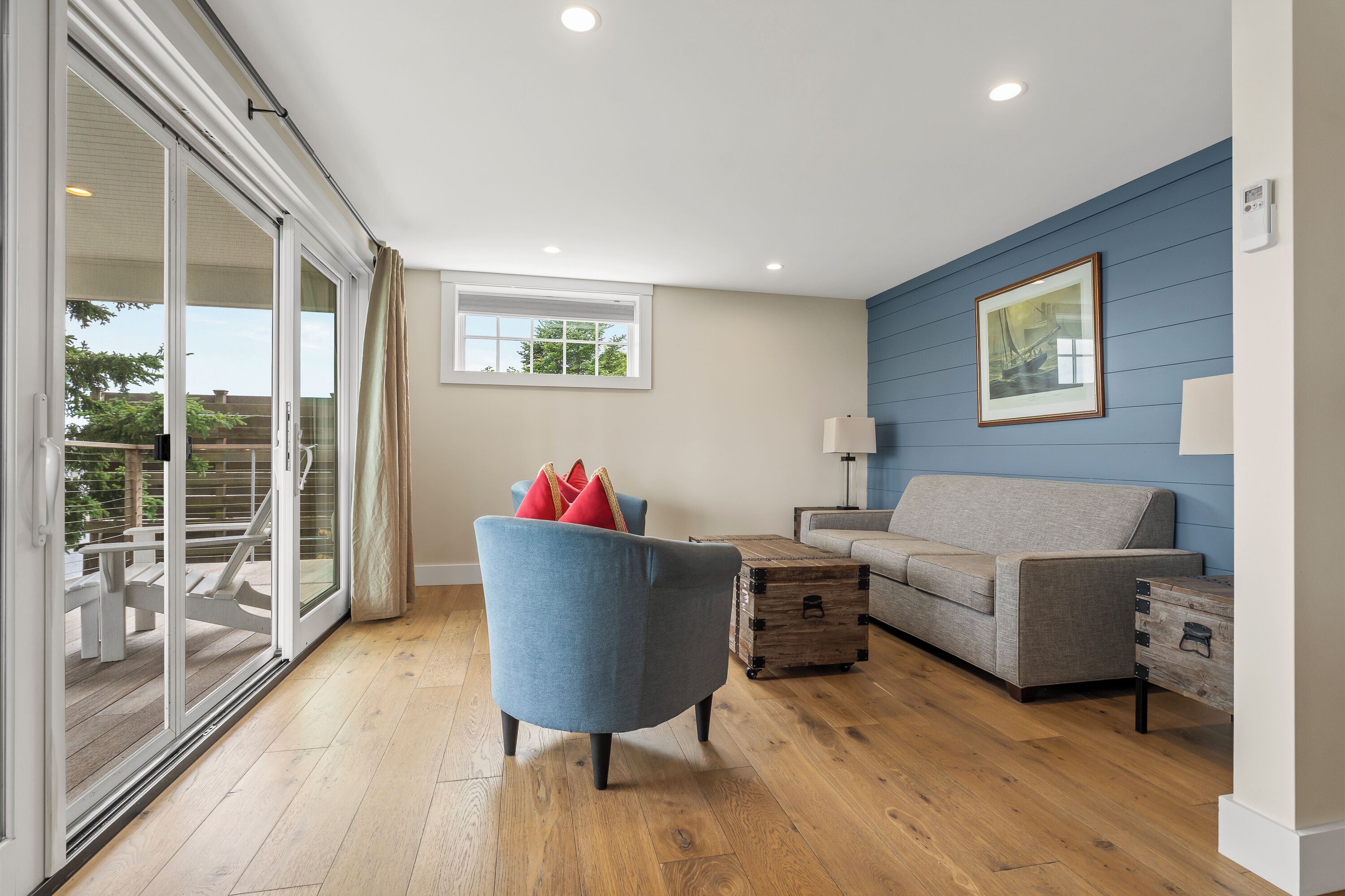 A modern living room with a blue sofa, a blue armchair, a wooden coffee table, and a large window with a view of greenery.