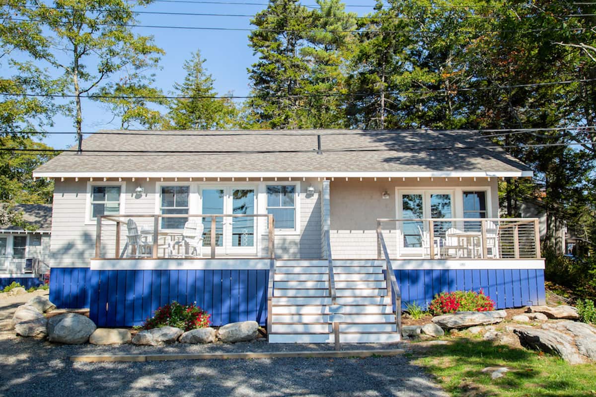 Une maison à deux étages avec une façade bleue, un porche à l’avant doté de chaises et une petite terrasse.