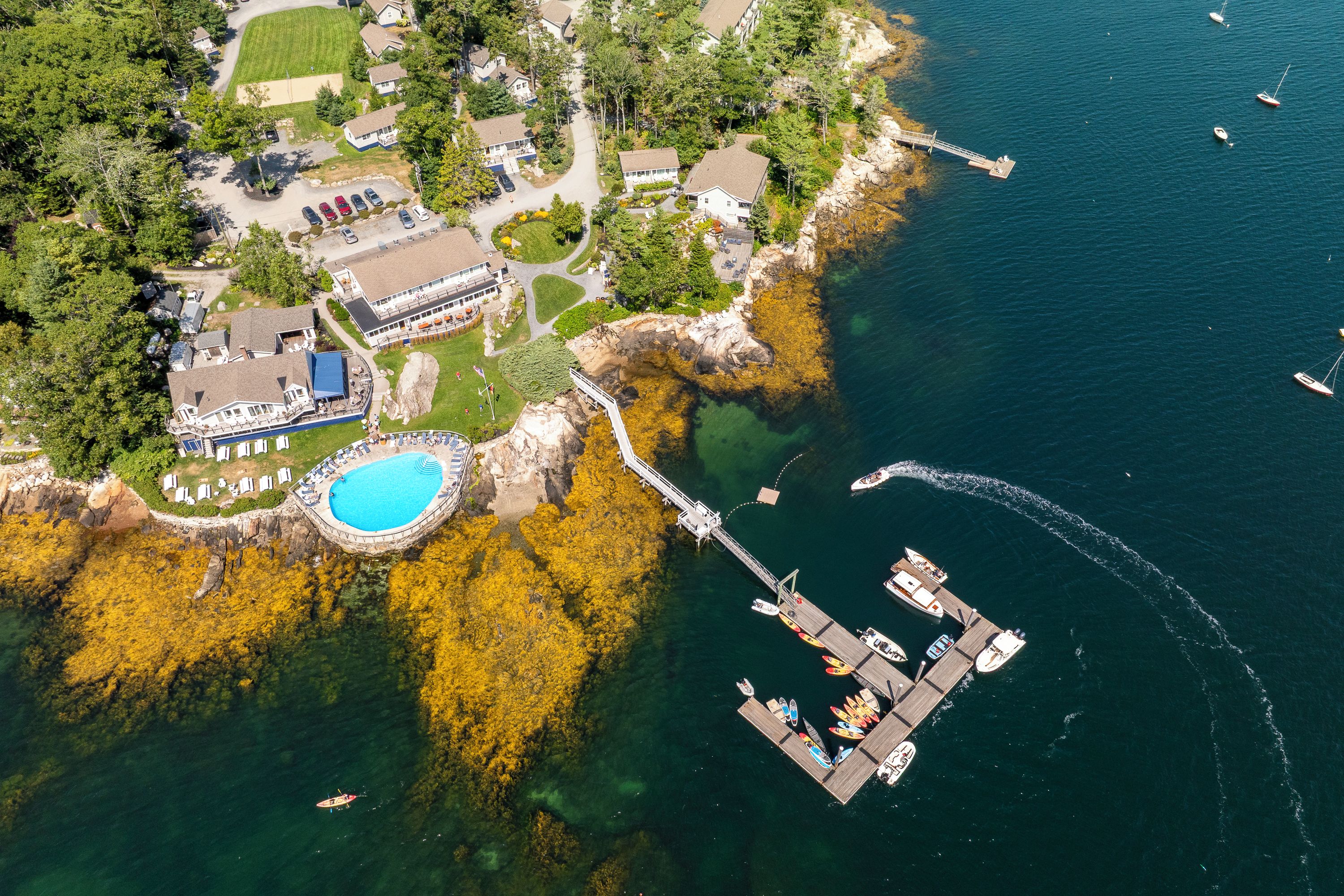 Vista aérea de uma propriedade costeira com piscina, um cais com barcos e um edifício grande com varanda.