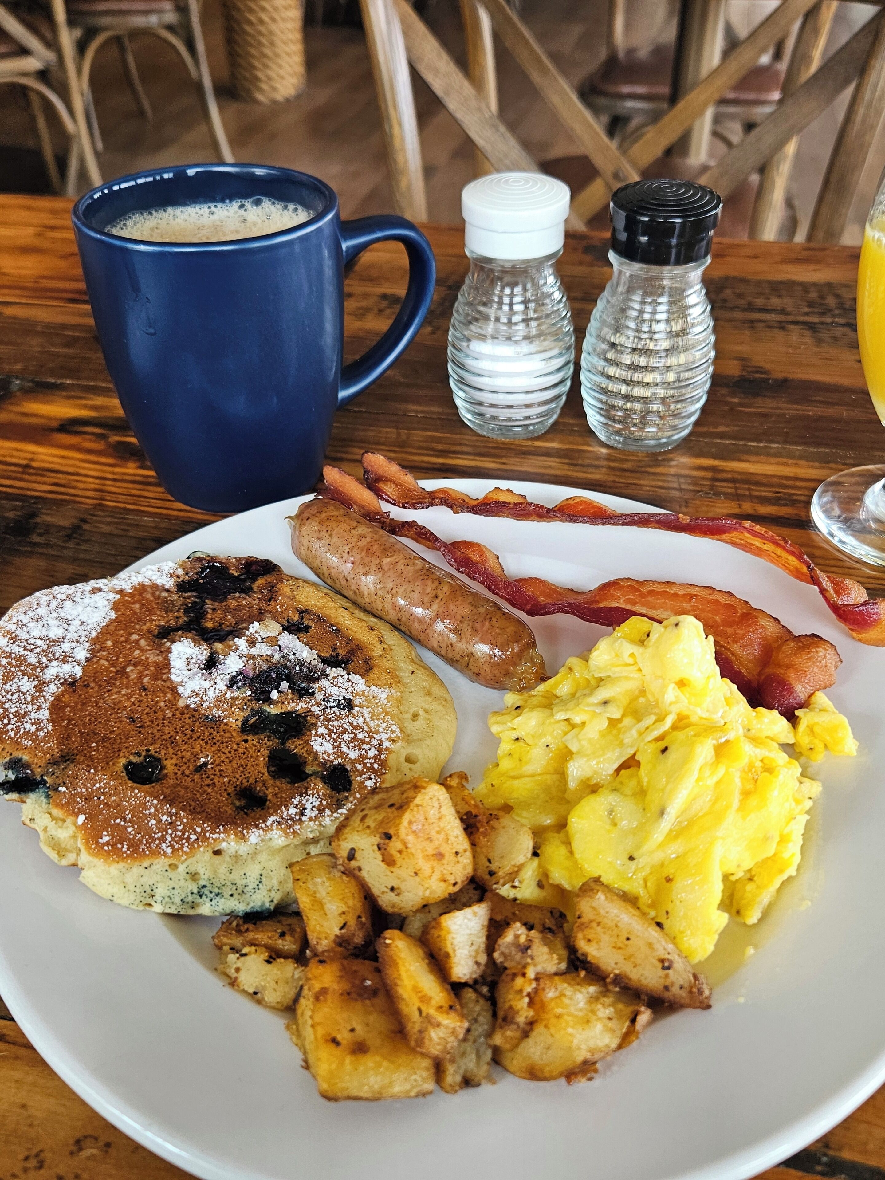 A breakfast plate with pancakes, sausages, bacon, scrambled eggs, and potatoes.