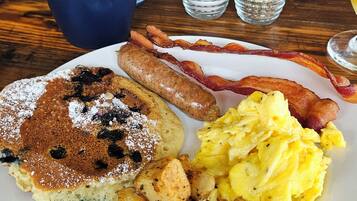 A breakfast plate with pancakes, sausages, bacon, scrambled eggs, and potatoes.