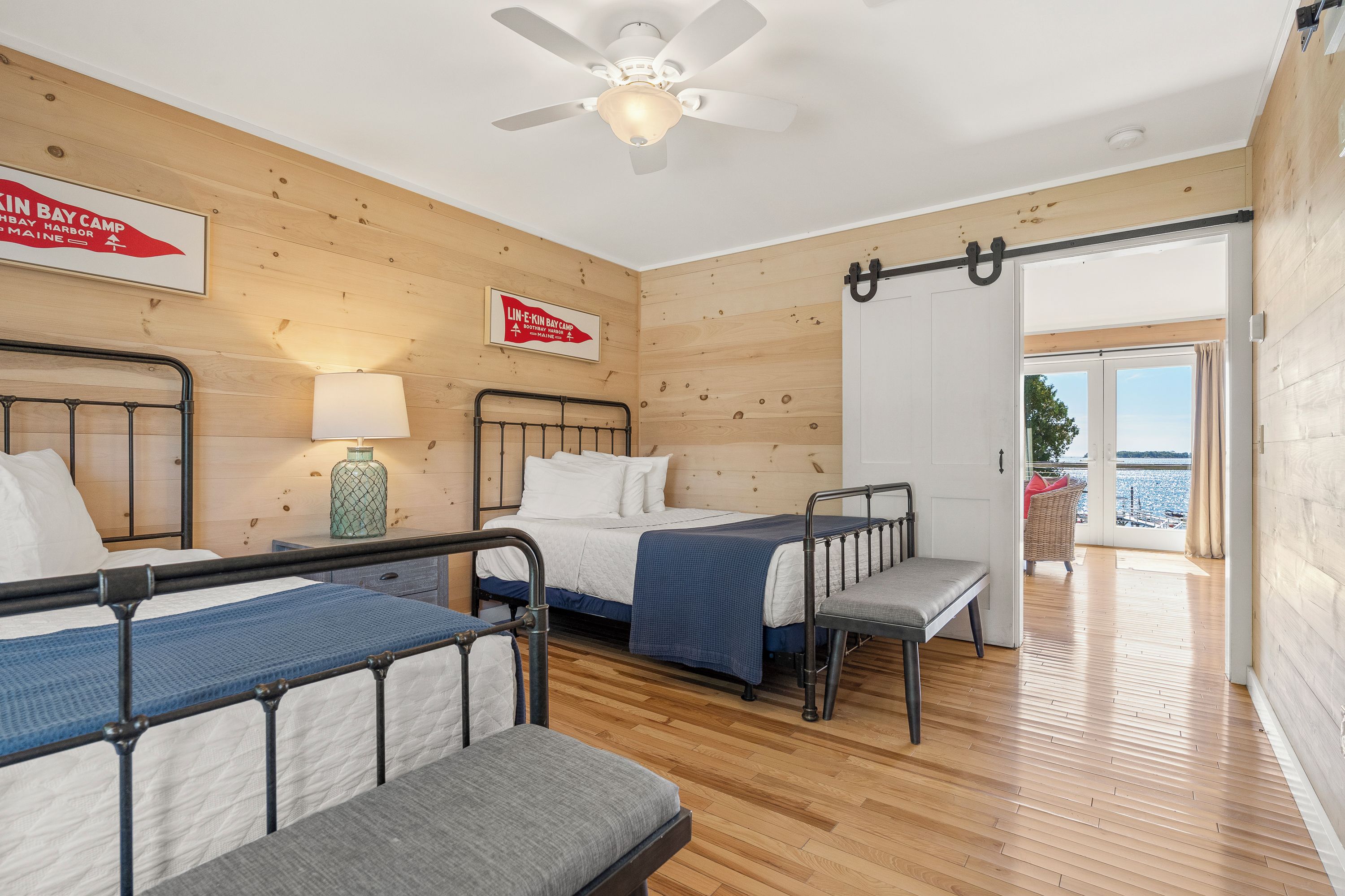 A room with two beds, a ceiling fan, a lamp, and a sign indicating a location.