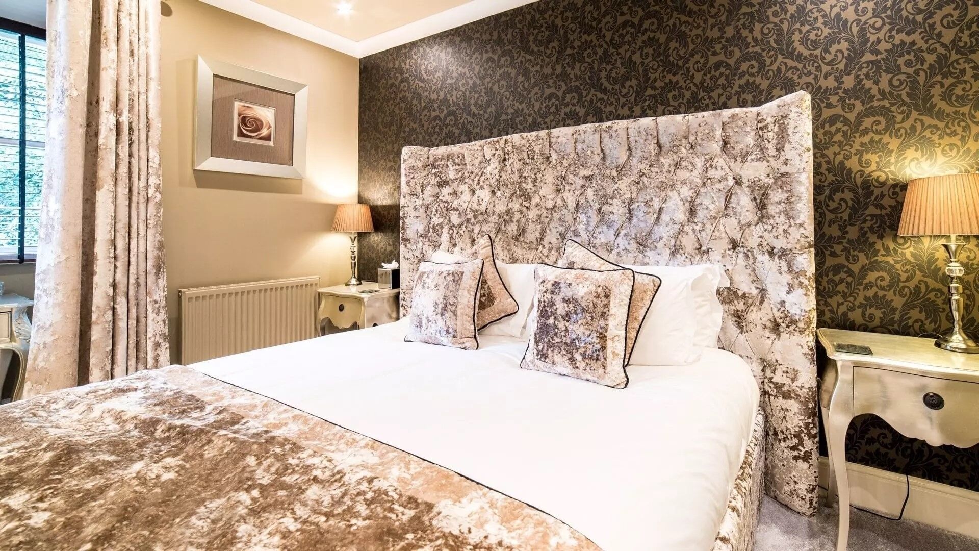 Un dormitorio con una cama grande, cabecera de estampado floral, dos lámparas de noche y un cuadro en la pared.