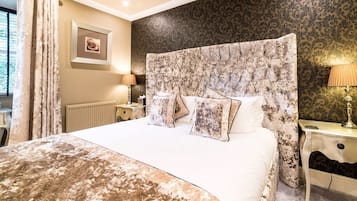 Un dormitorio con una cama grande, cabecera de estampado floral, dos lámparas de noche y un cuadro en la pared.