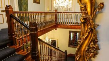 Un magnifique escalier orné d’un lustre, un balcon au deuxième étage et un grand miroir décoratif.