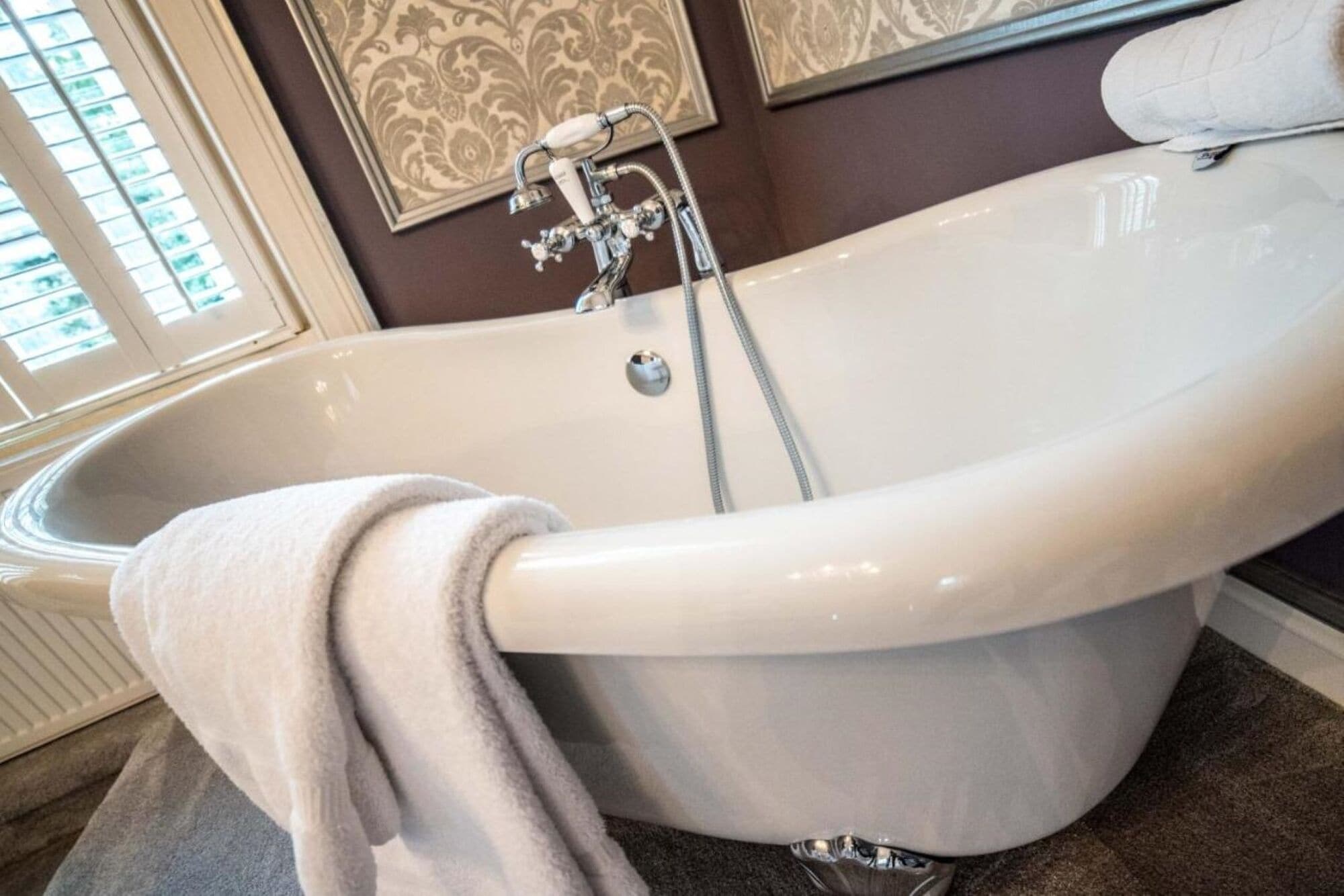 A freestanding bathtub with a shower head and a towel draped over it.