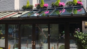 Una entrada amb envidrac i una catifa vermella, un rètol que diu "Berry Manor" i plantes en testos a la teulada.