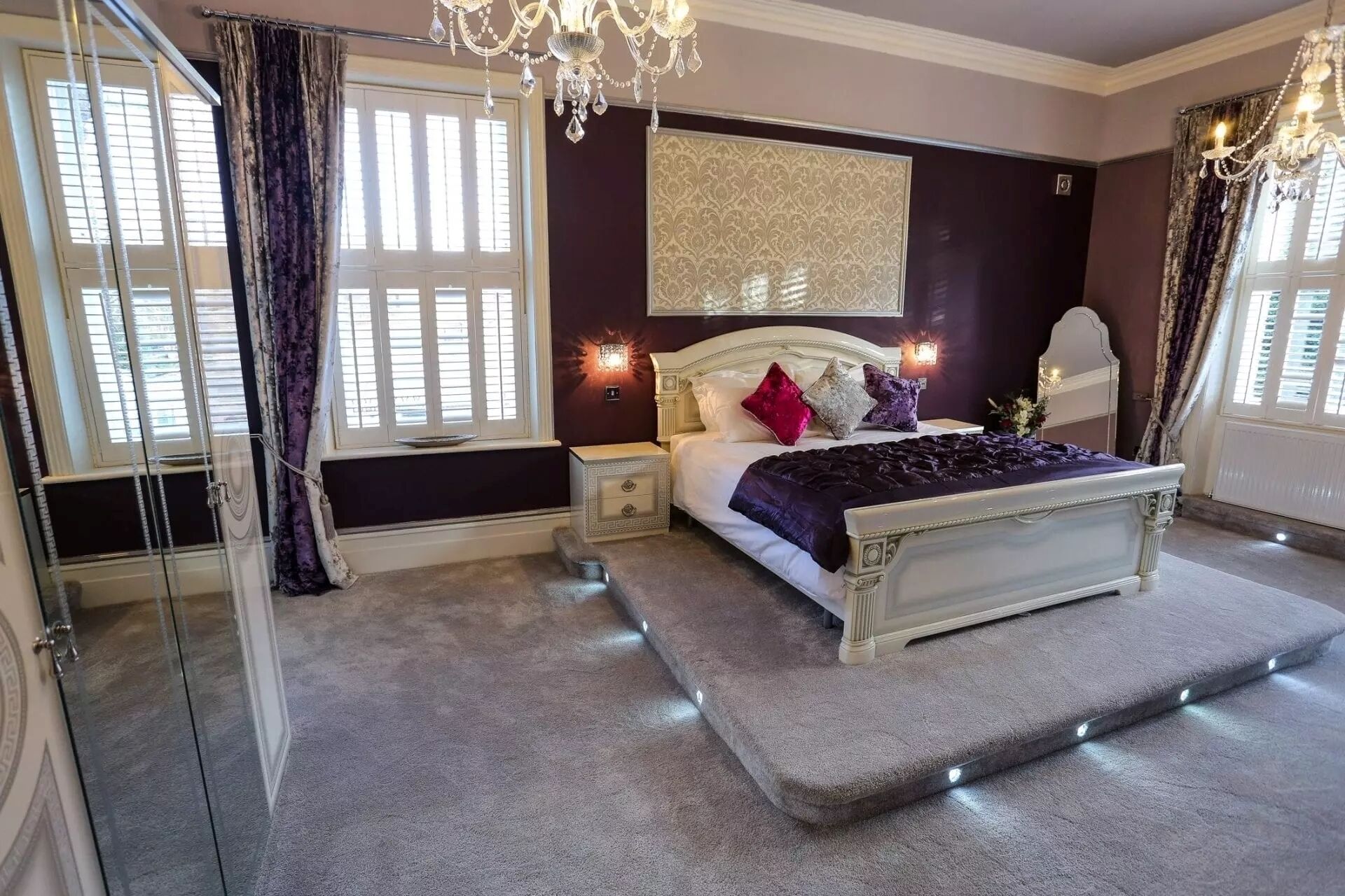 A bedroom with a large bed, a nightstand, a dresser, and a chandelier.