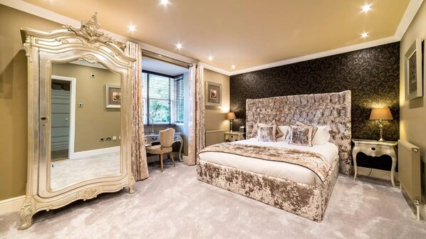 A bedroom with a large ornate mirror, a tufted headboard bed, a desk, and a chair.