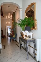 Een gang met een kroonluchter, een spiegel, een potplant en een klein tafeltje met decoratieve objecten.