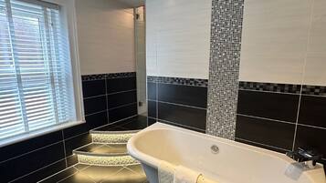 Ein modernes Badezimmer mit einer freistehenden Badewanne, Wänden mit schwarz-weißen Fliesen und einem Fenster mit Jalousien.