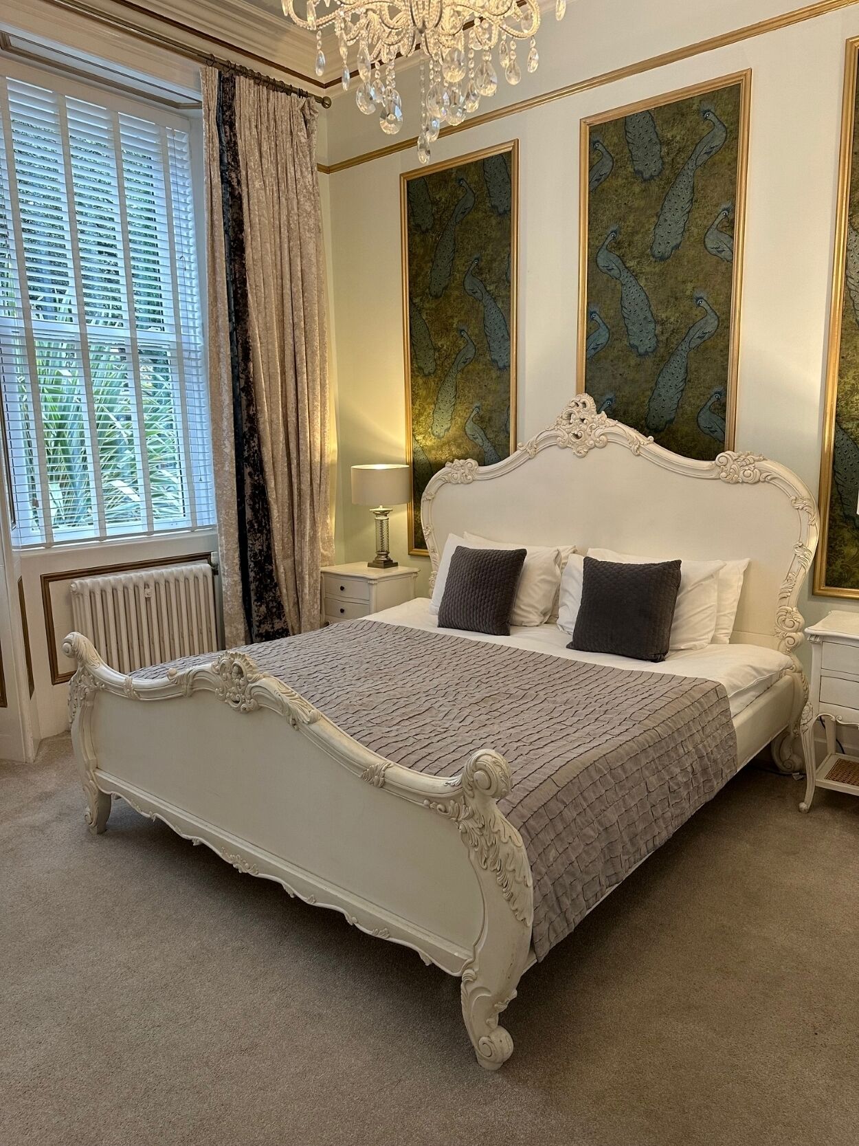 A classic bedroom with a large bed, ornate headboard, and two wall paintings.