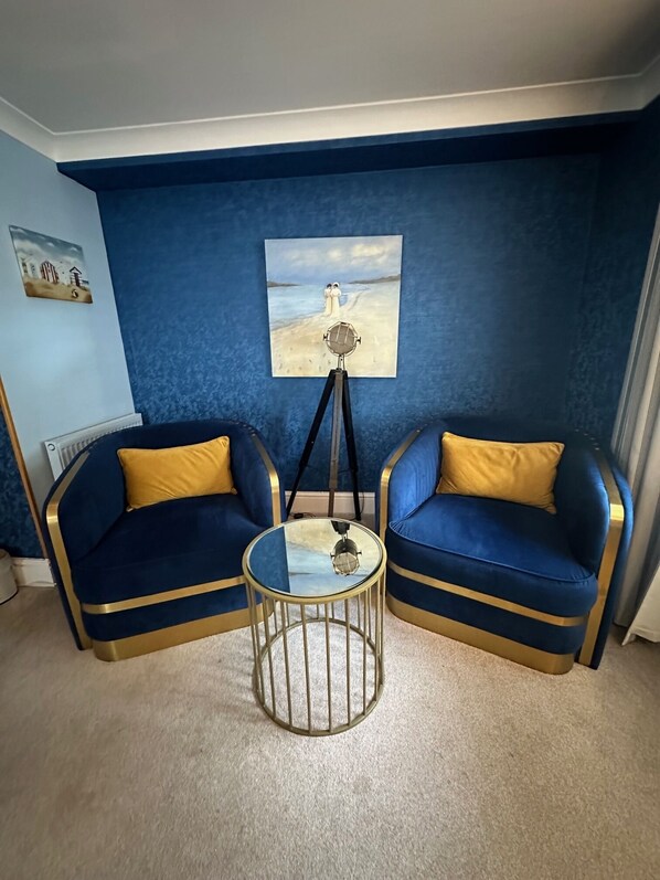 A room with two blue sofas with gold trim, a small round table, and a painting on the wall. - Derby Manor (Bournemouth)
