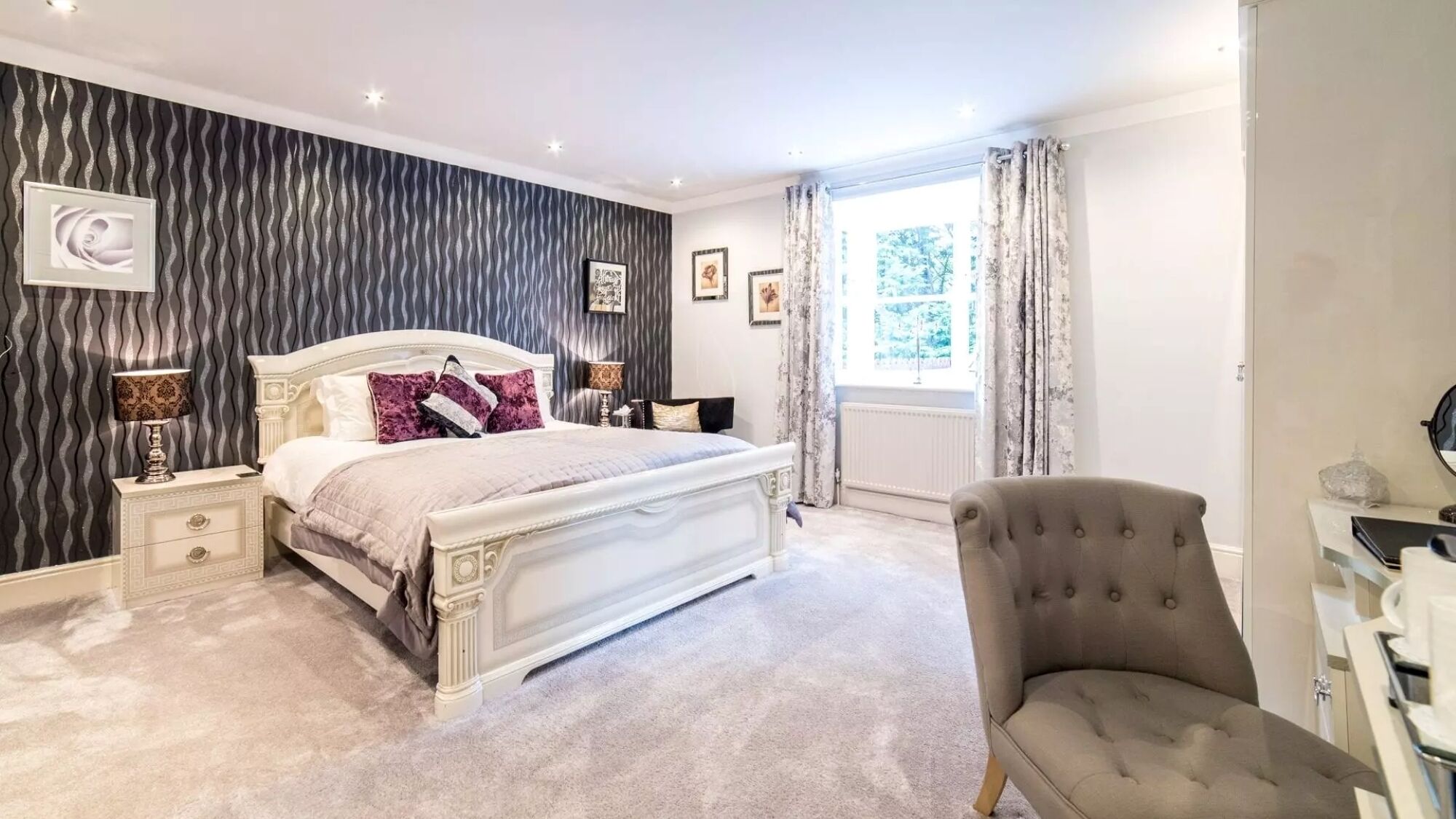 A bedroom with a large bed, a chair, a nightstand, and a window with curtains.