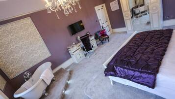A bedroom with a large bed, a white bathtub, a television, and a chandelier.