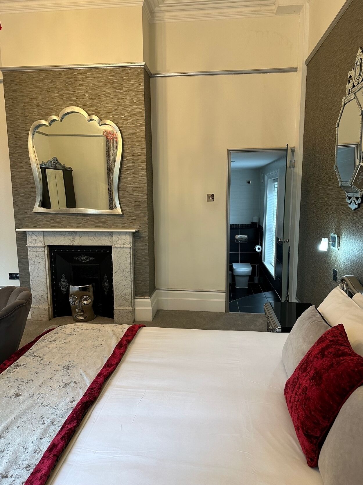 A bedroom with a large bed, a fireplace, a mirror, and a bathroom visible through an open door.