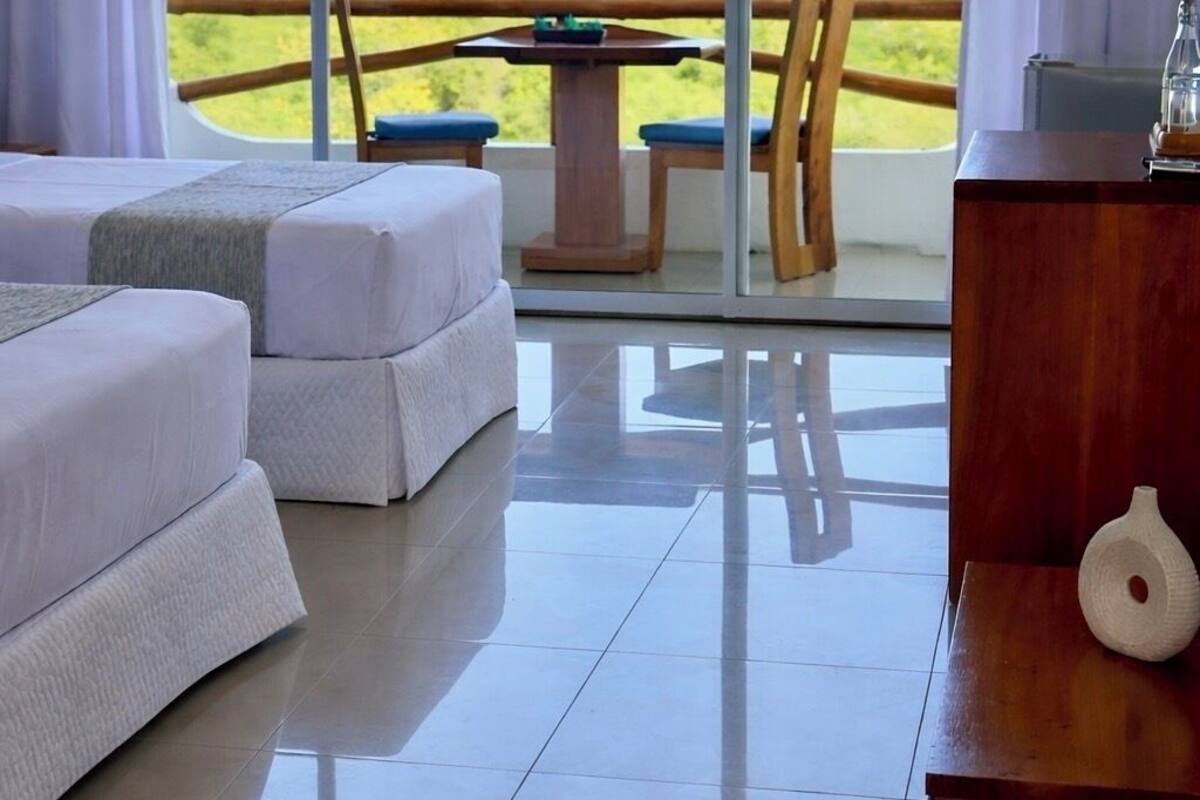 A room with a bed, a table, chairs, and a view of the sea.