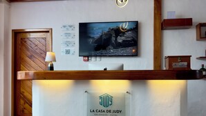 A hotel reception desk with a mounted television, a sign reading 'LA CASA DE JUDY GALÁPAGOS - HOTEL,' and a wooden door. - Hotel La Casa de Judy (Puerto Ayora)