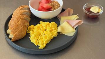 A plate with scrambled eggs, watermelon, granola, ham, and a croissant on a table.