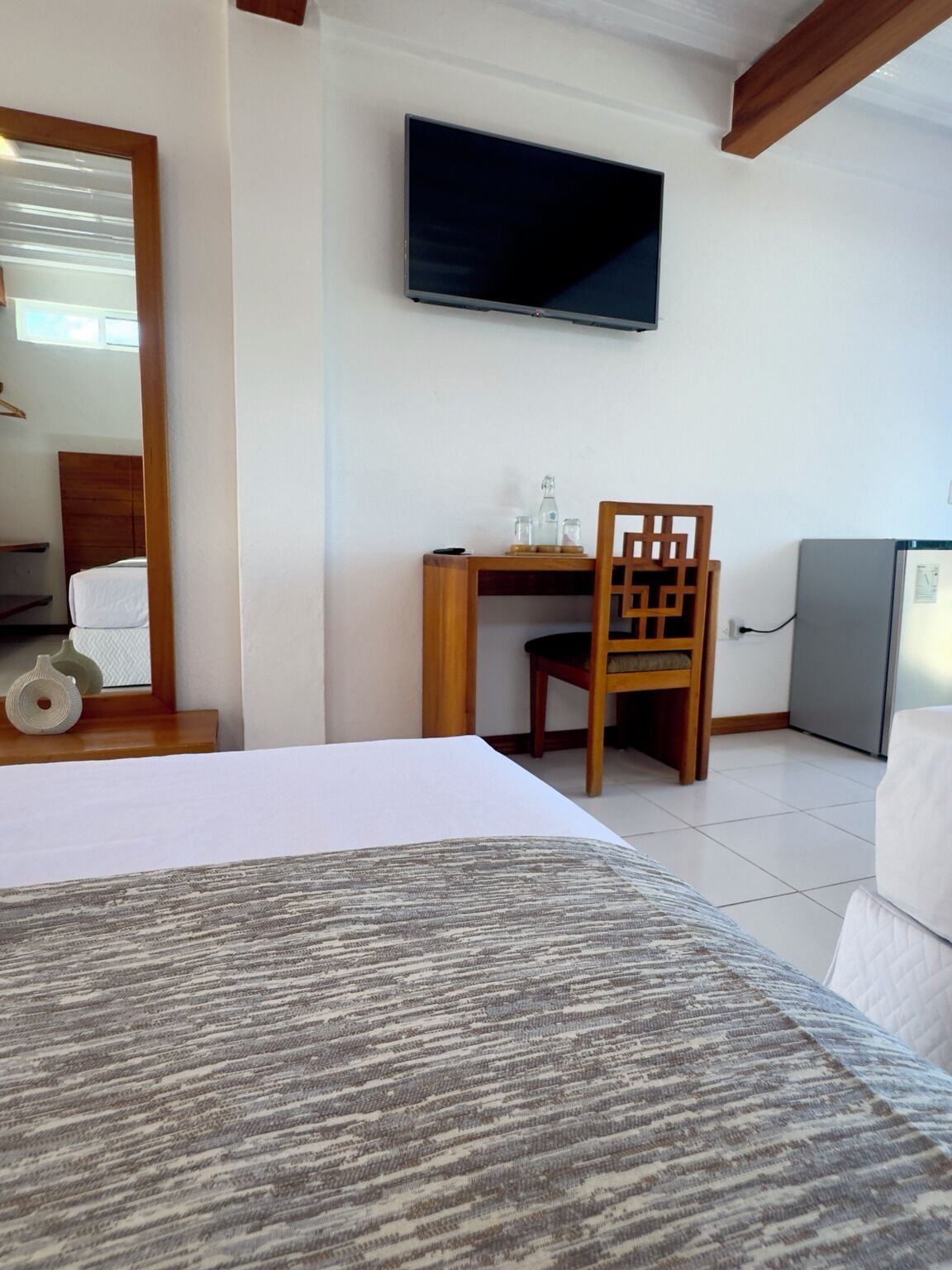 A hotel room with a bed, a desk, a chair, a television, and a refrigerator.